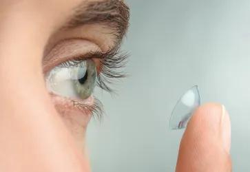 Foto zeigt eine Nahaufnahme eines Auges und einen Finger auf dem eine Kontaktlinse liegt