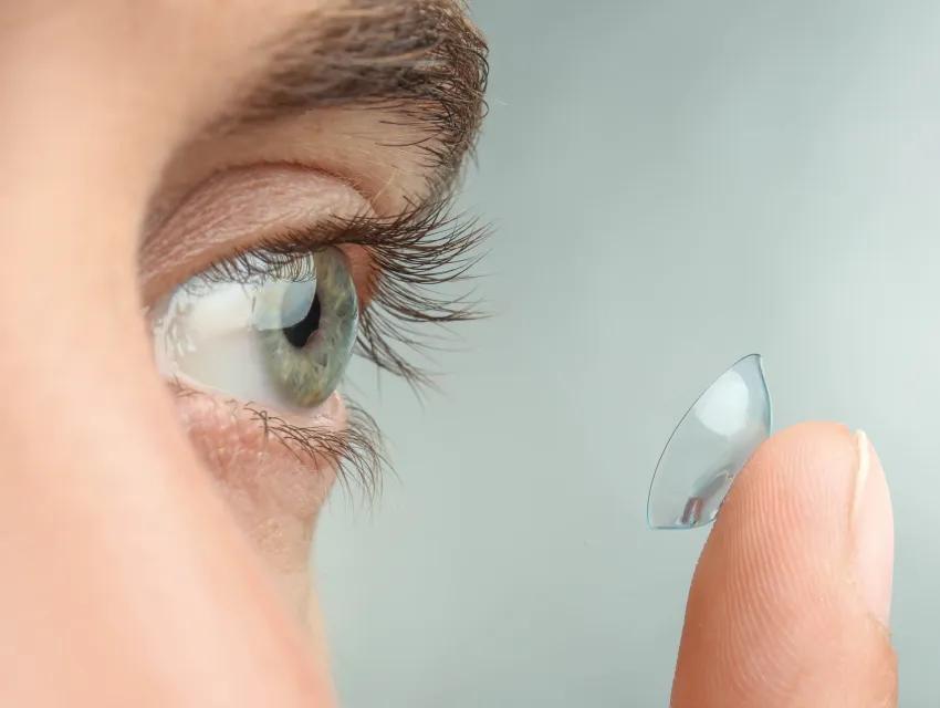 Foto zeigt eine Nahaufnahme eines Auges und einen Finger auf dem eine Kontaktlinse liegt