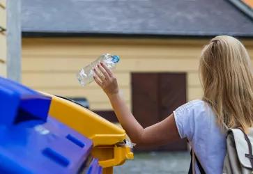 Frau recycled eine Plastikflasche im Container