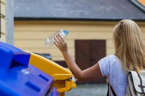 Frau recycled eine Plastikflasche im Container