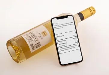 Foto einer Weinflasche mit E-Label und einem Smartphone, auf dessen Bildschirm Zutaten und Nährwerte des Weins zu sehen sind