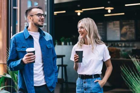Mann und Frau vor einem Café halten Mehrweg-to-go Becher in der Hand