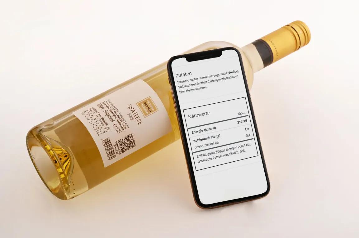 Foto einer Weinflasche mit E-Label und einem Smartphone, auf dessen Bildschirm Zutaten und Nährwerte des Weins zu sehen sind