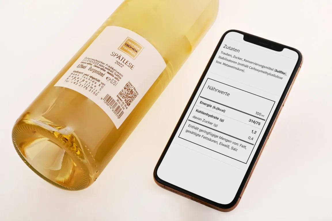 Foto einer Weinflasche mit E-Label und einem Smartphone, auf dessen Bildschirm Zutaten und Nährwerte des Weins zu sehen sind