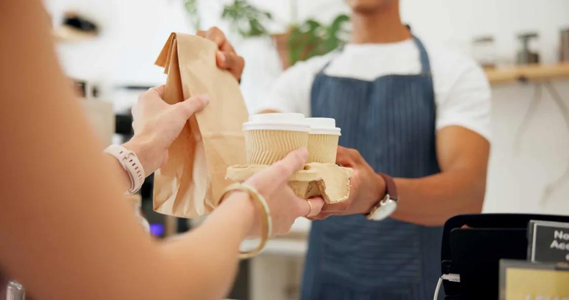 Barista reicht Coffee-to-go-Becher über die Theke