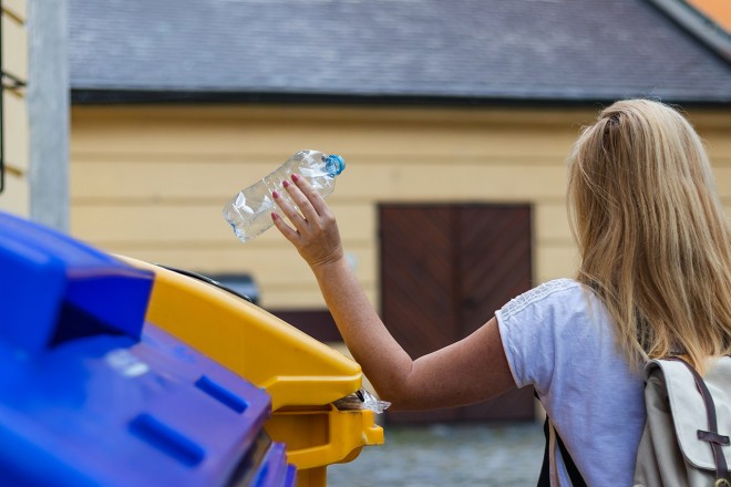 Frau recycled eine Plastikflasche im Container