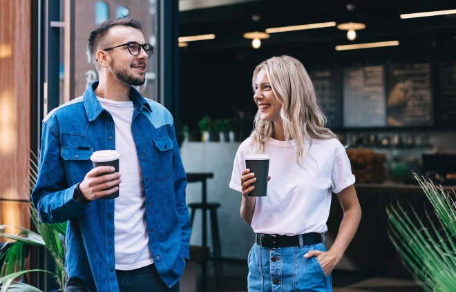 Mann und Frau vor einem Café halten Mehrweg-to-go Becher in der Hand